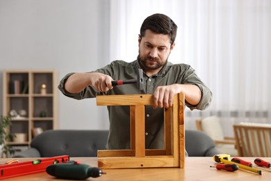 Photo of Man repairing wooden stool with nail and hammer at home