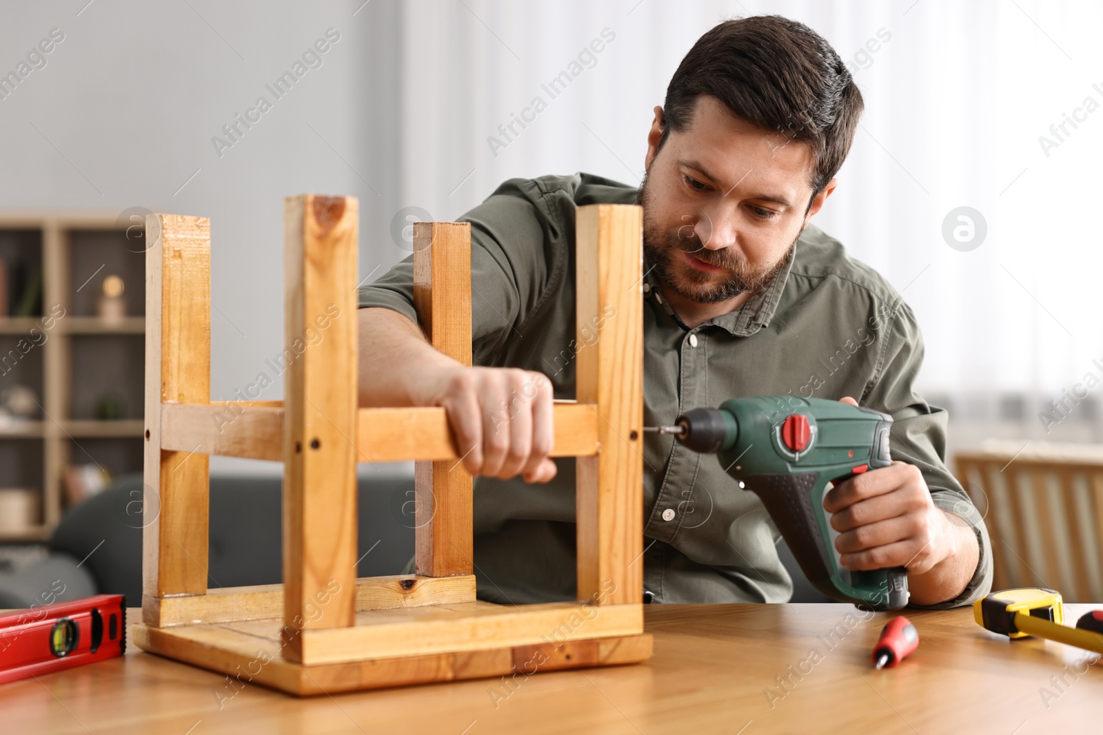 Photo of Man repairing wooden stool with electric screwdriver at home