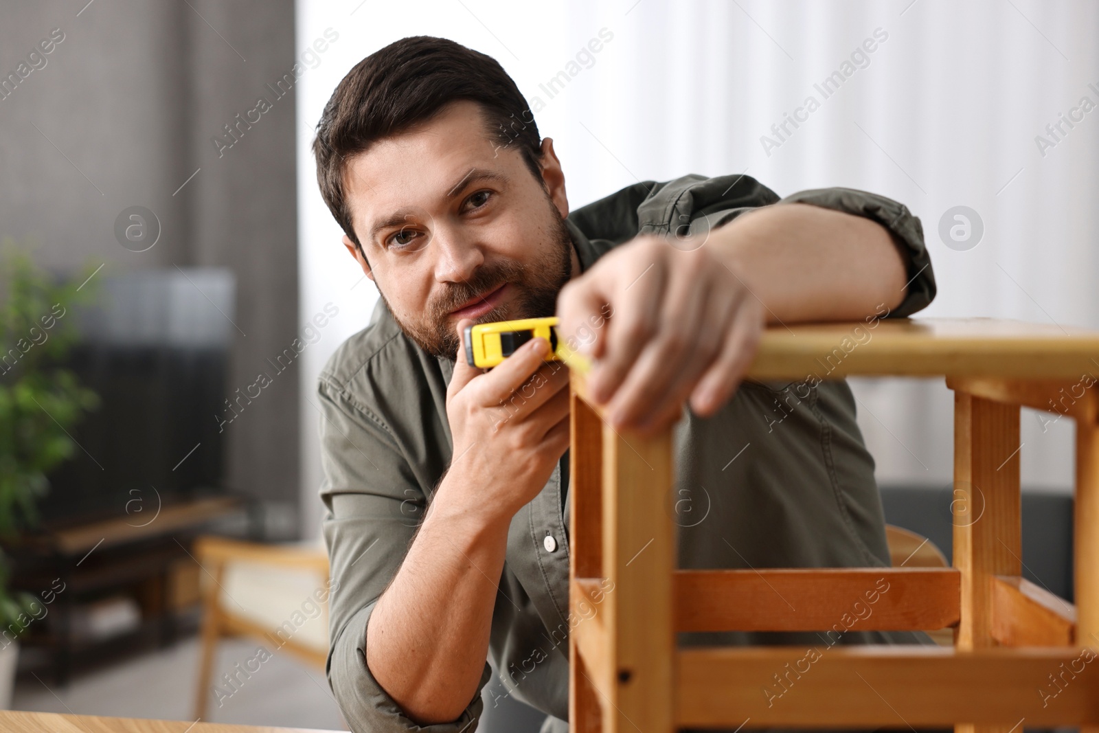 Photo of Man using tape measure while repairing wooden stool at home