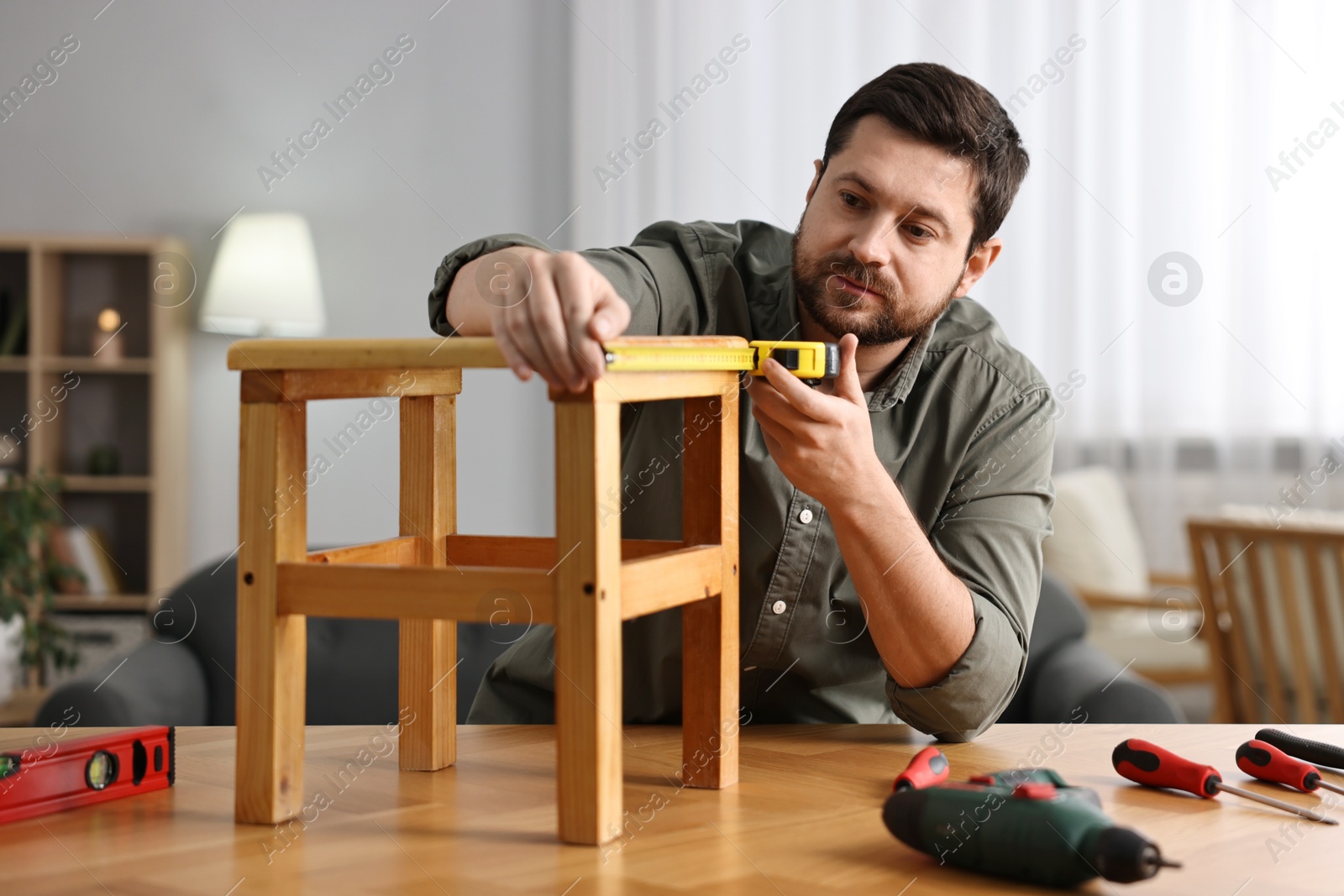 Photo of Man using tape measure while repairing wooden stool at home