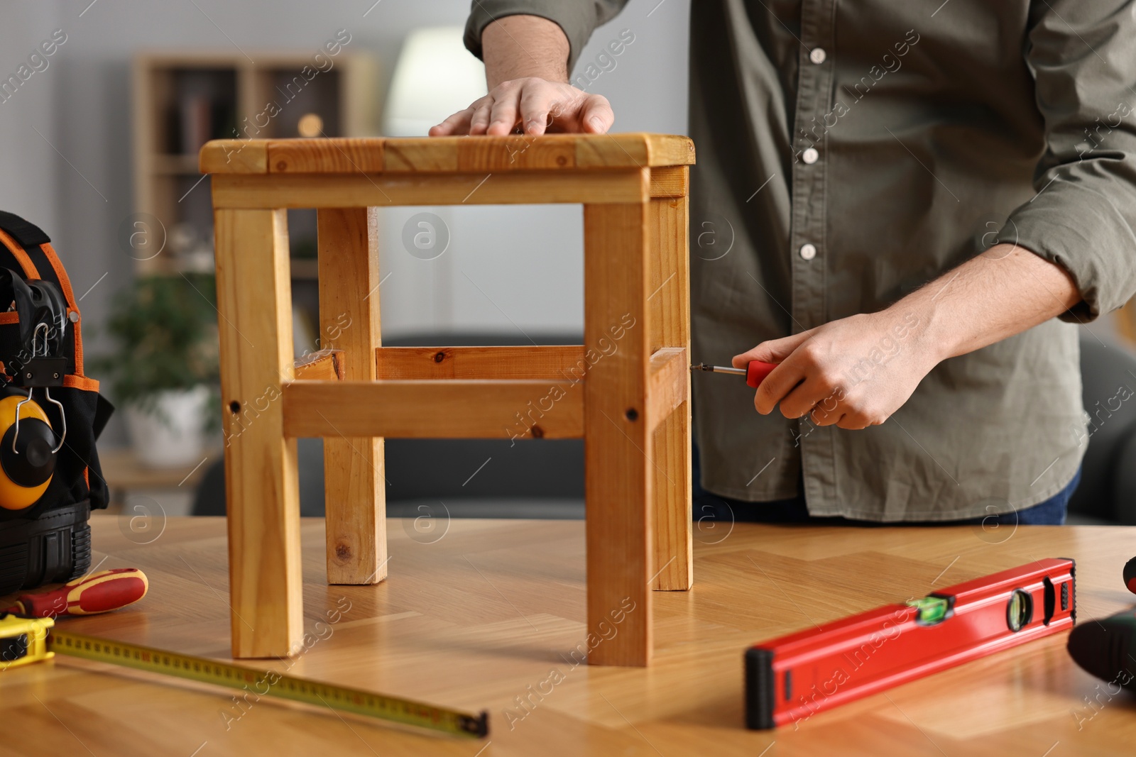 Photo of Man repairing wooden stool with screwdriver at home, closeup