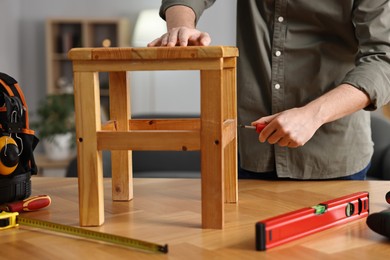 Photo of Man repairing wooden stool with screwdriver at home, closeup