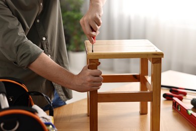 Photo of Man repairing wooden stool with screwdriver at home, closeup