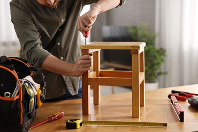 Photo of Man repairing wooden stool with screwdriver at home, closeup