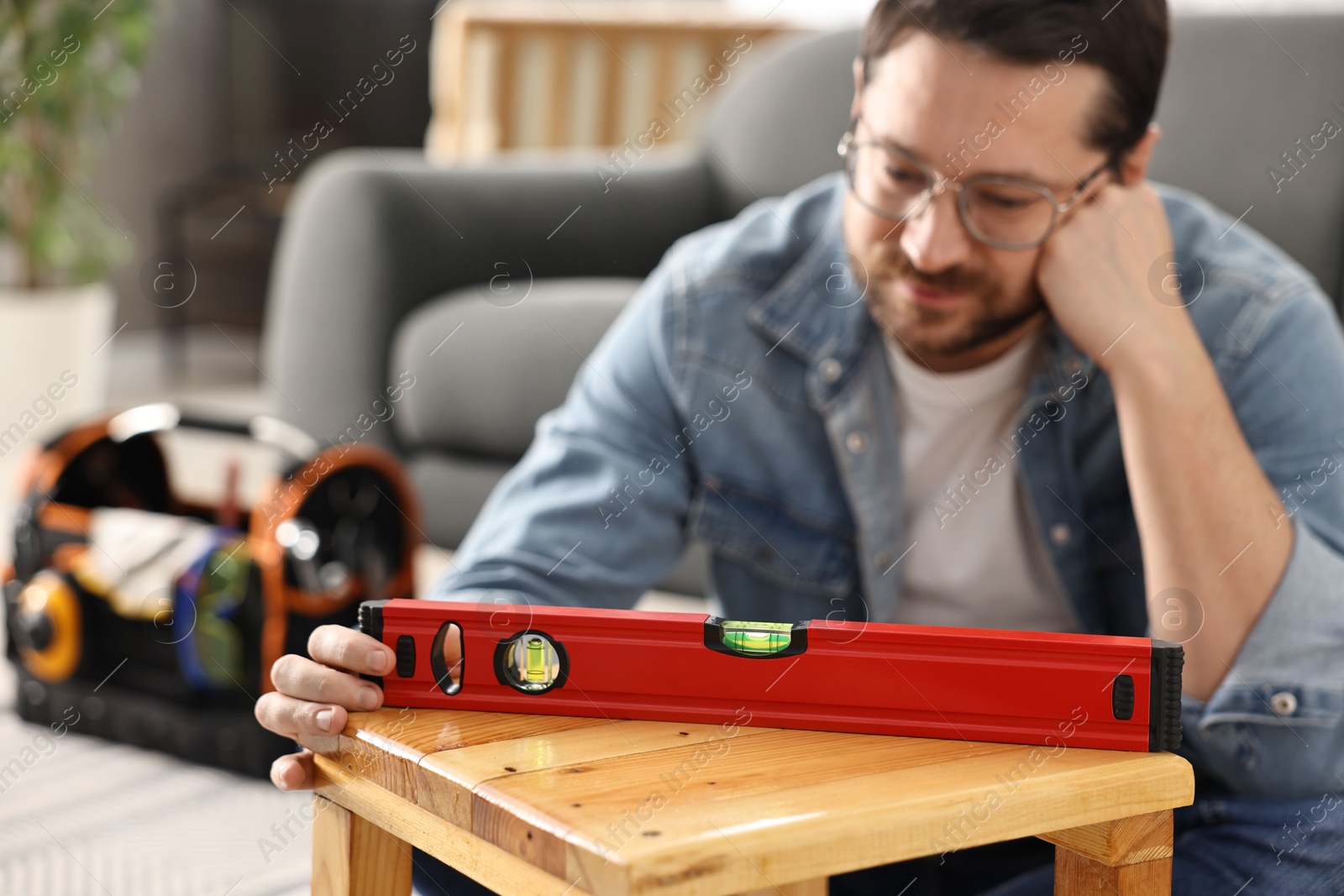 Photo of Man using level tool while repairing wooden stool at home, selective focus