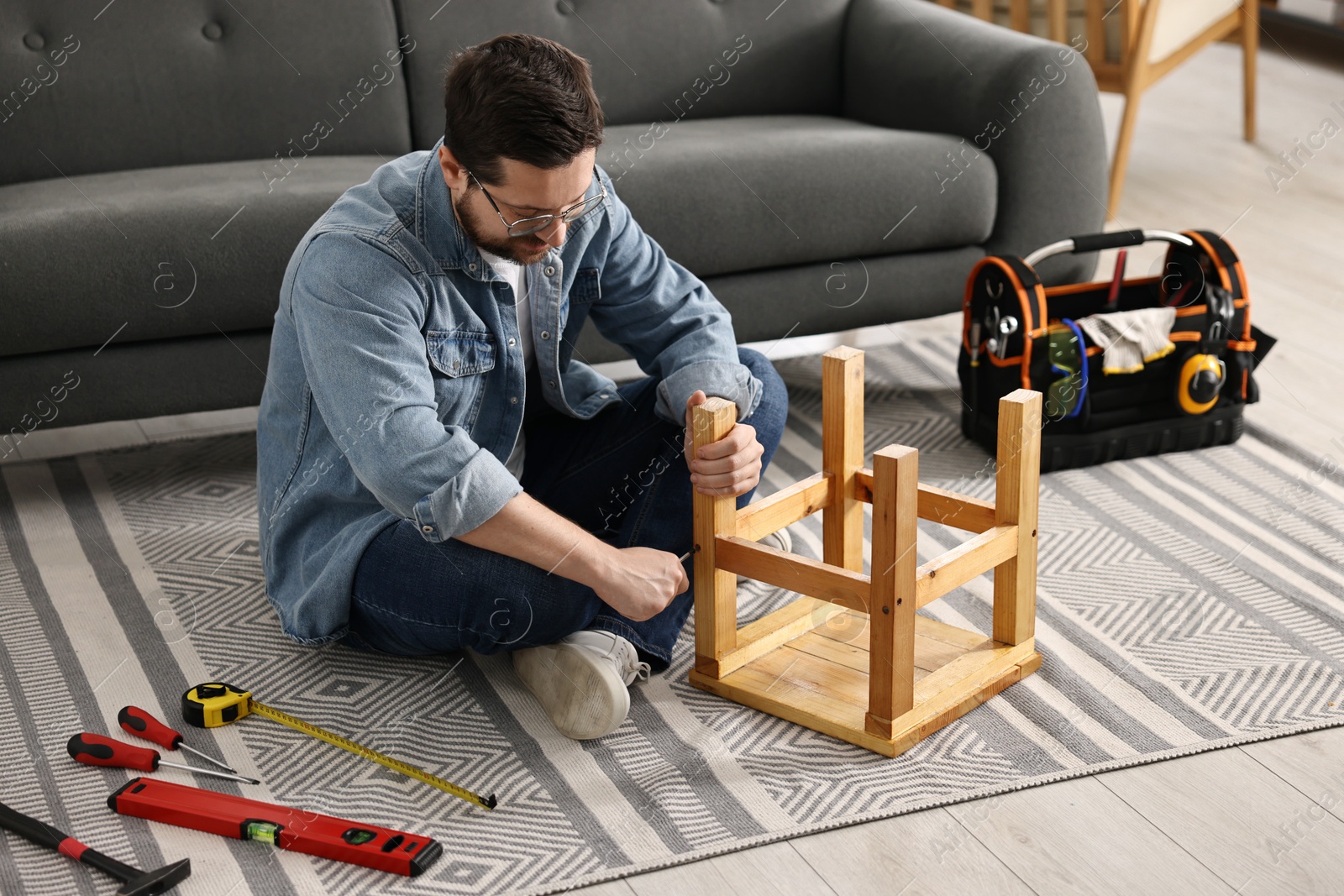 Photo of Man repairing wooden stool with screwdriver at home