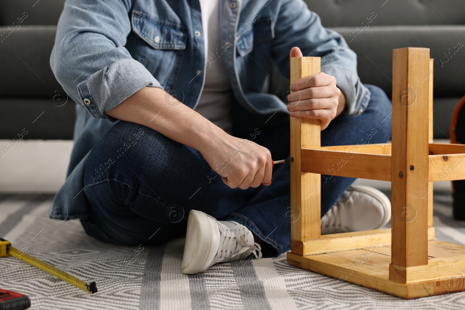 Photo of Man repairing wooden stool with screwdriver at home, closeup