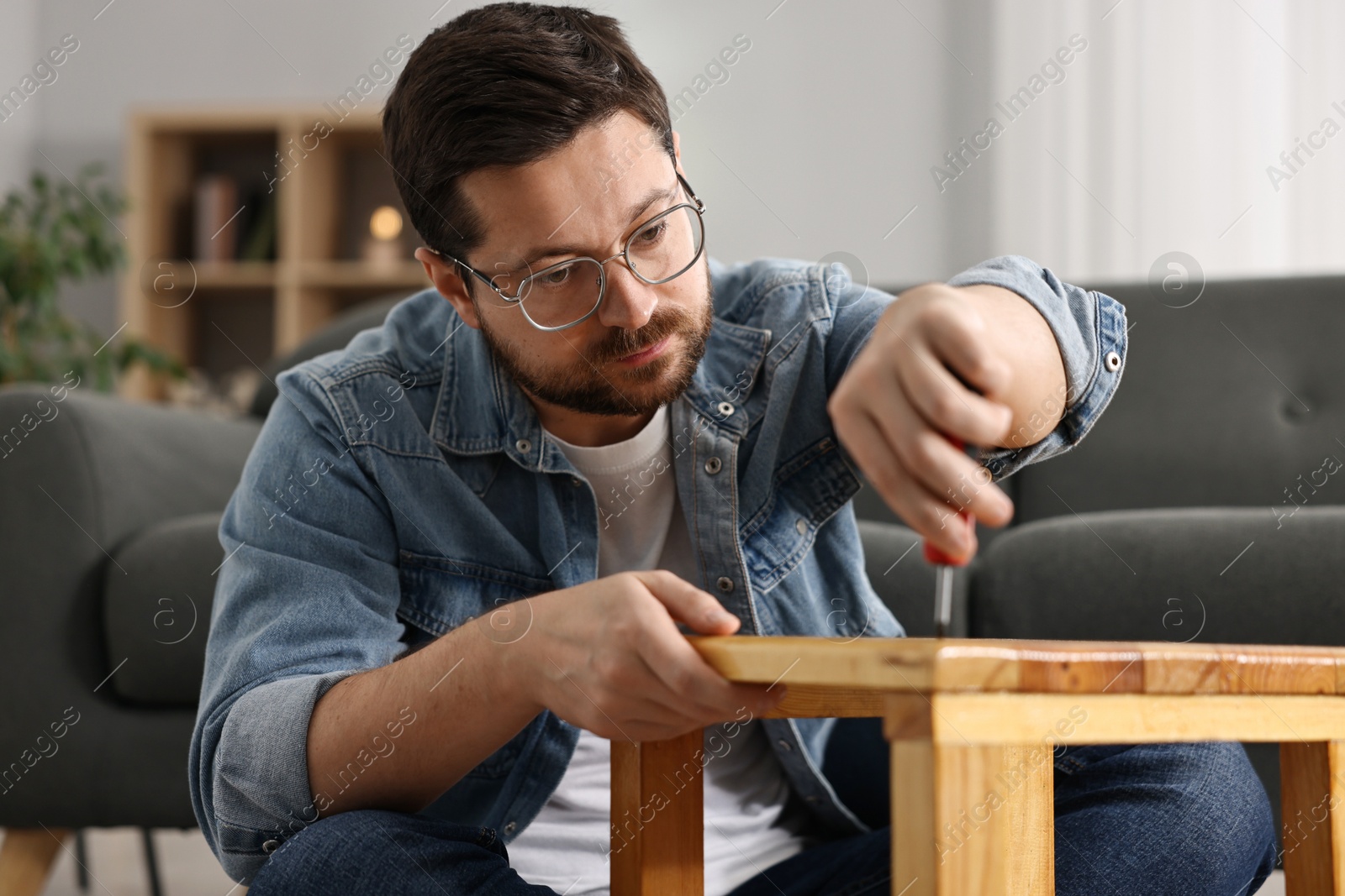 Photo of Man repairing wooden stool with screwdriver at home