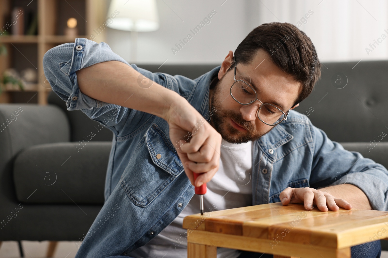 Photo of Man repairing wooden stool with screwdriver at home