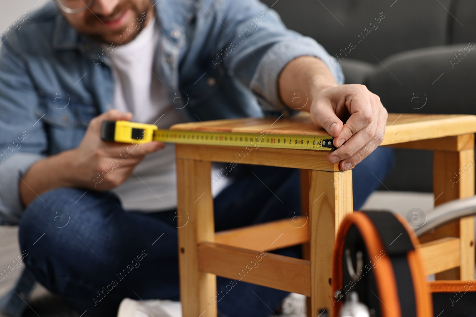 Photo of Man using tape measure while repairing wooden stool at home, closeup