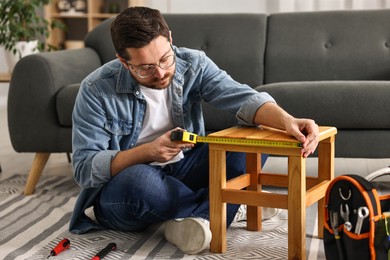 Photo of Man using tape measure while repairing wooden stool at home