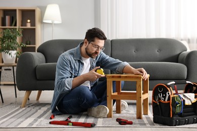 Photo of Man using tape measure while repairing wooden stool at home