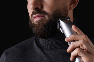 Photo of Man trimming beard on black background, closeup