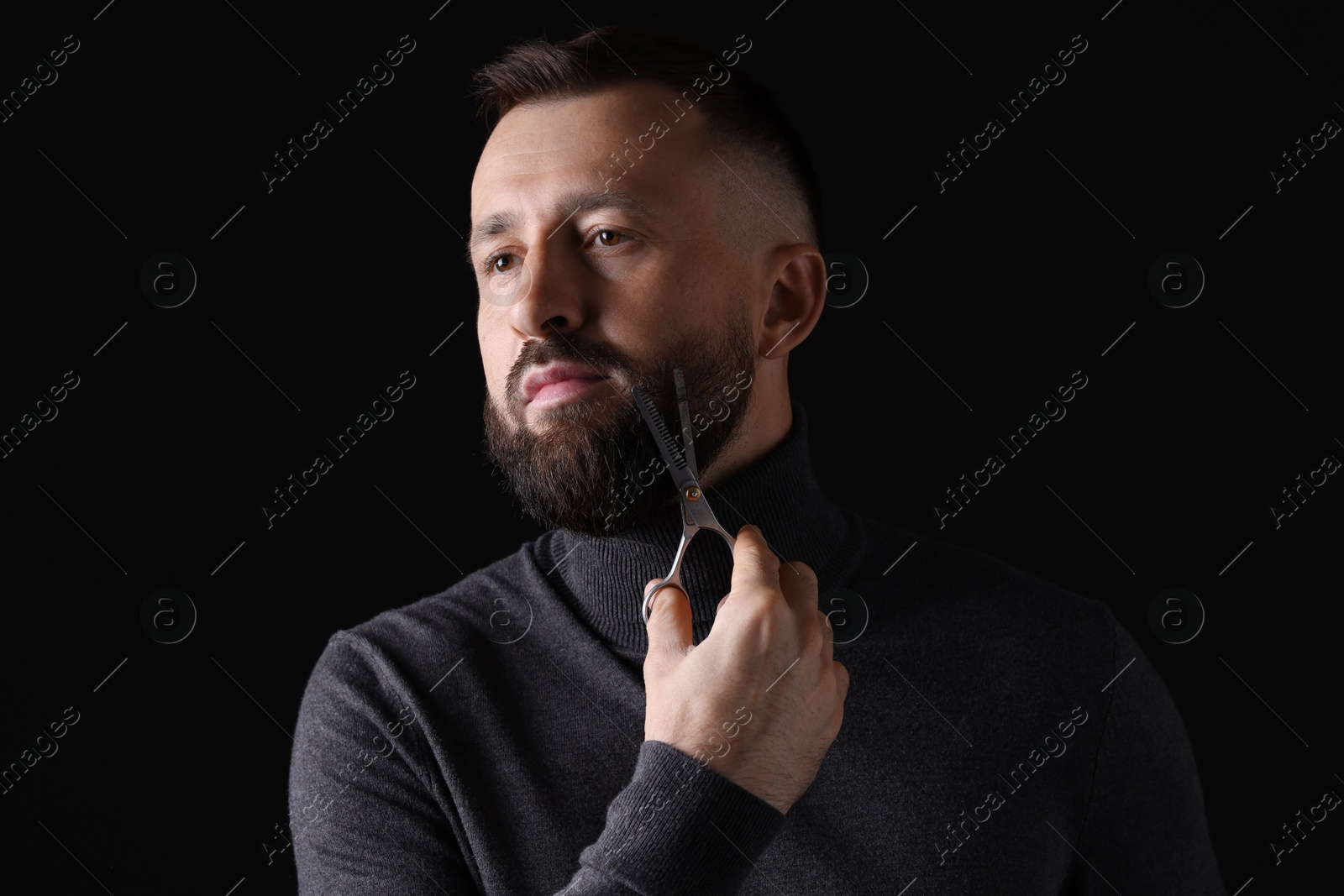 Photo of Man trimming beard with scissors on black background