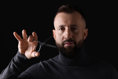 Photo of Bearded man holding scissors on black background