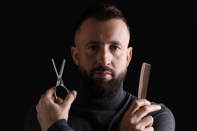 Photo of Bearded man holding comb and scissors on black background