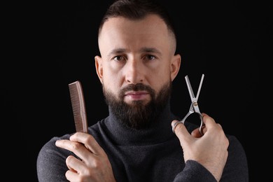 Photo of Bearded man holding comb and scissors on black background