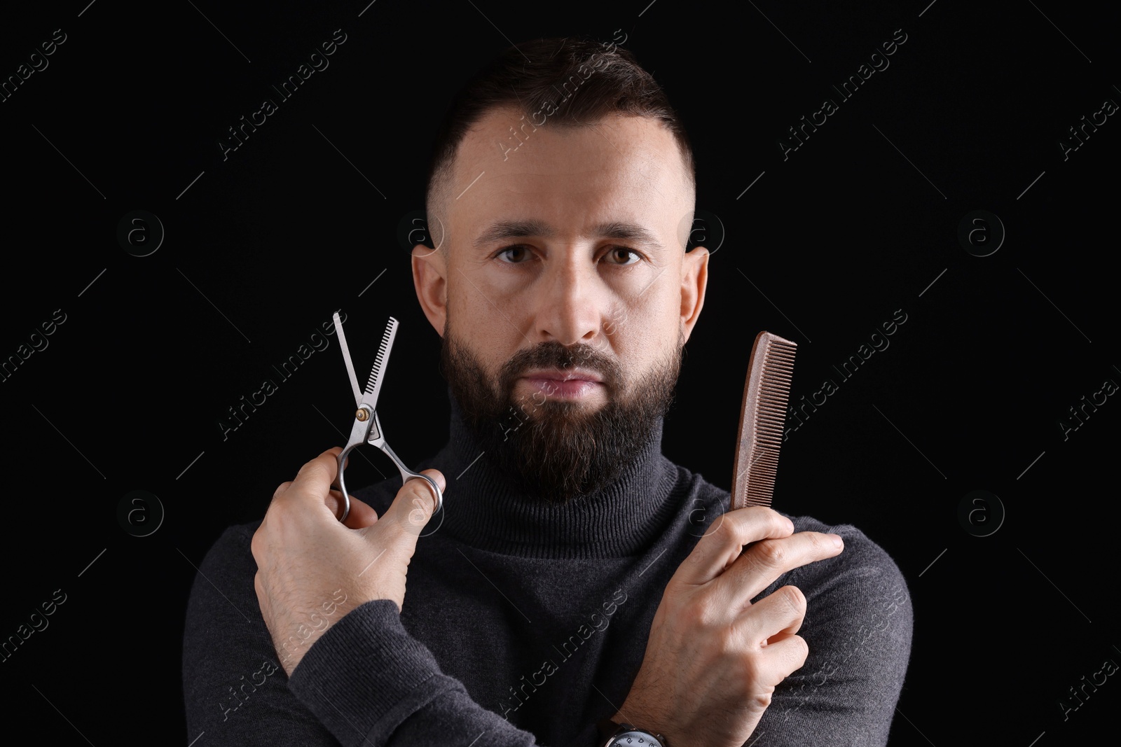 Photo of Bearded man holding comb and scissors on black background