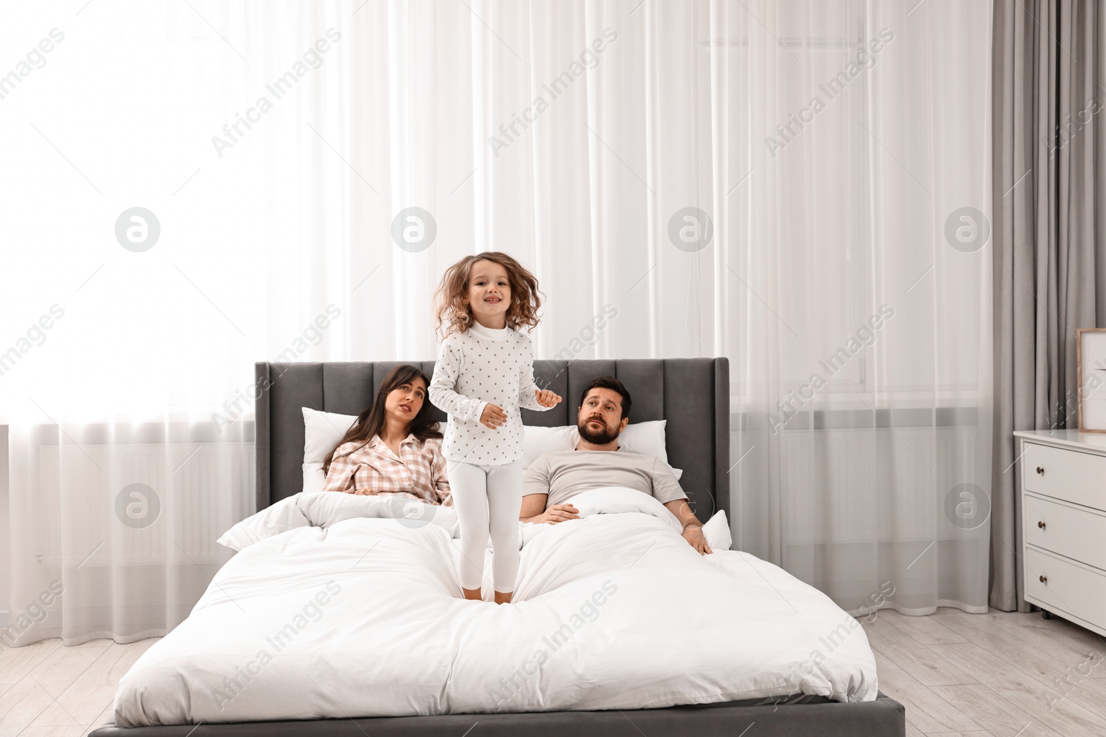 Photo of Happy playful daughter and her overwhelmed parents on bed at home