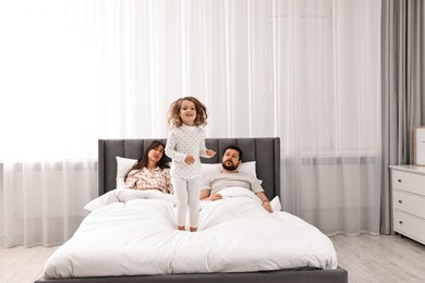 Photo of Happy playful daughter and her overwhelmed parents on bed at home