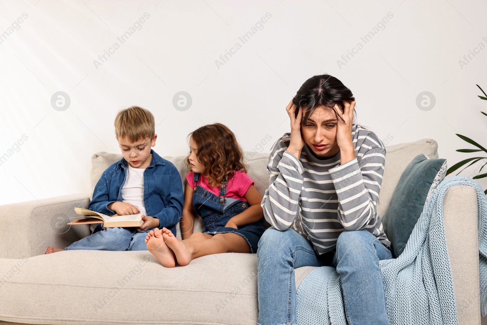 Photo of Overwhelmed mother and her naughty children with book on sofa at home