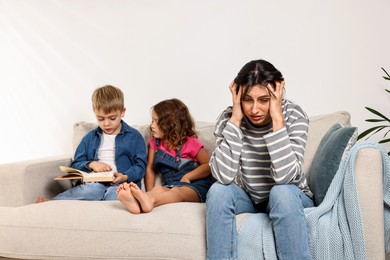 Photo of Overwhelmed mother and her naughty children with book on sofa at home