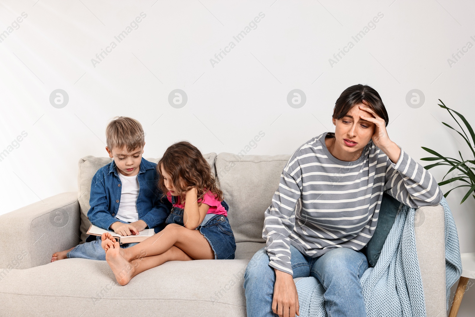 Photo of Overwhelmed mother and her naughty children with book on sofa at home