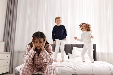 Photo of Overwhelmed mother and her playful children on bed at home