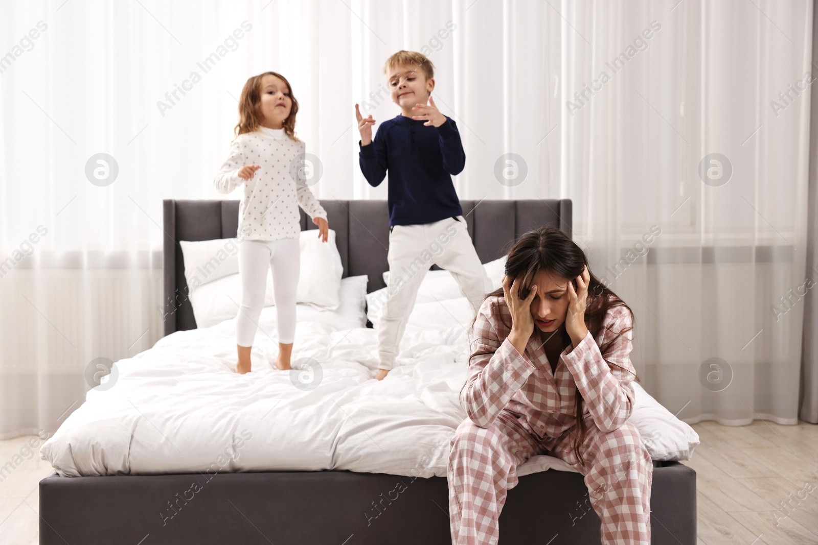 Photo of Overwhelmed mother and her playful children on bed at home