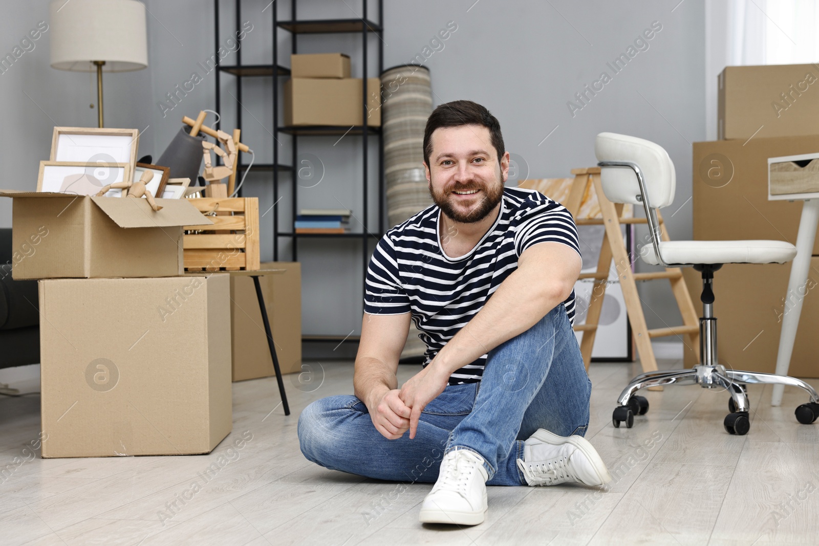 Photo of Moving day. Man resting on floor near cardboard boxes in his new home