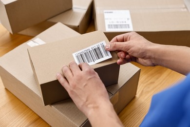 Photo of Man sticking barcode on parcel at wooden table indoors, closeup