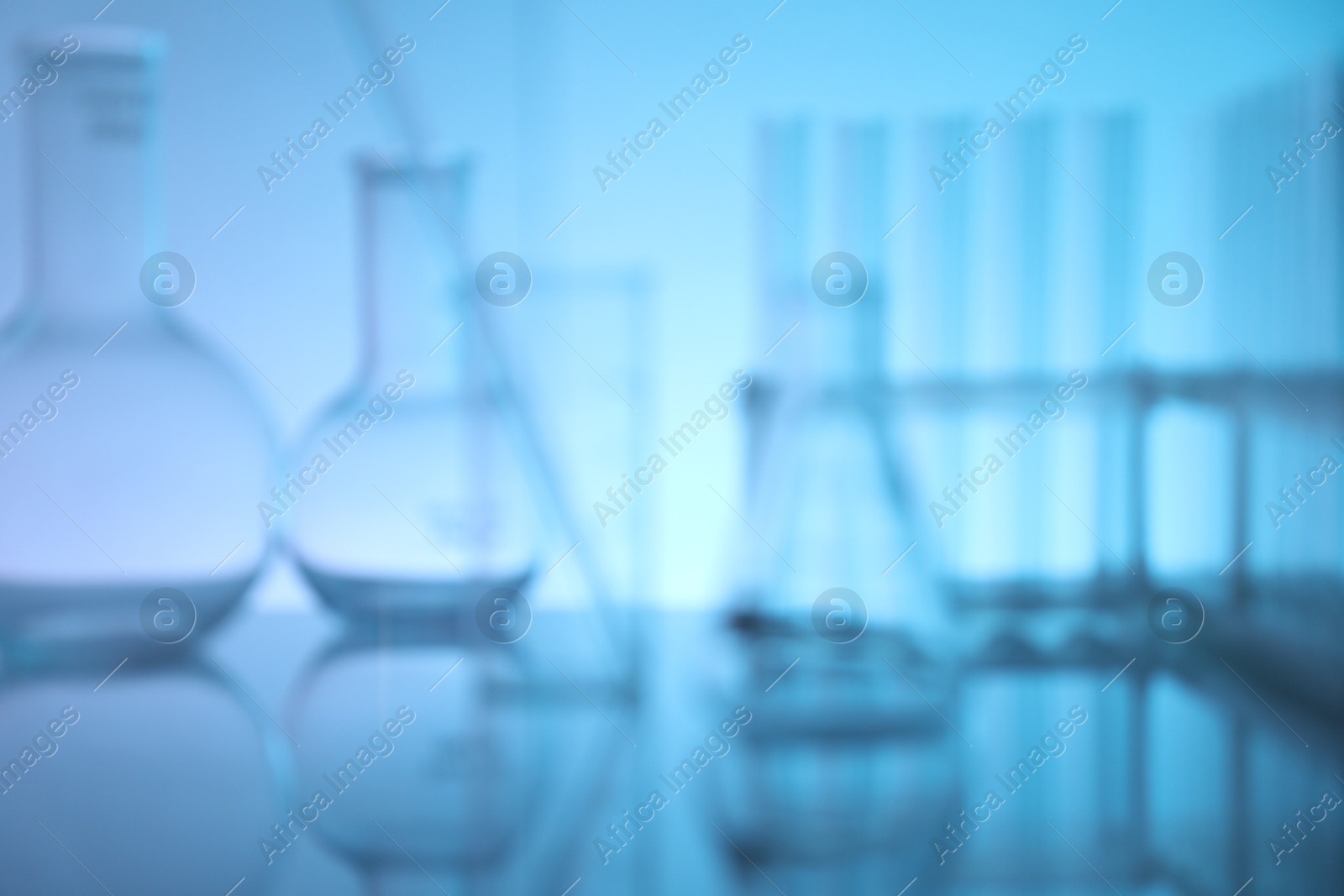 Photo of Blurred view of laboratory glassware on mirror surface against light blue background