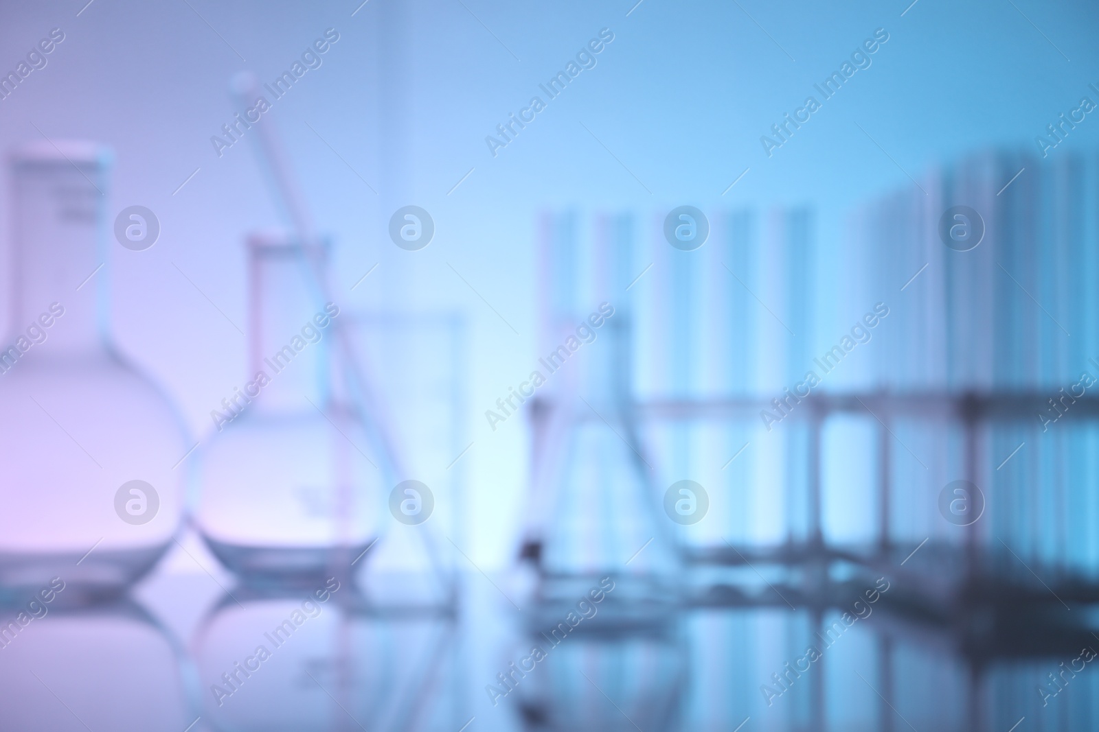 Photo of Blurred view of laboratory glassware on mirror surface against color background