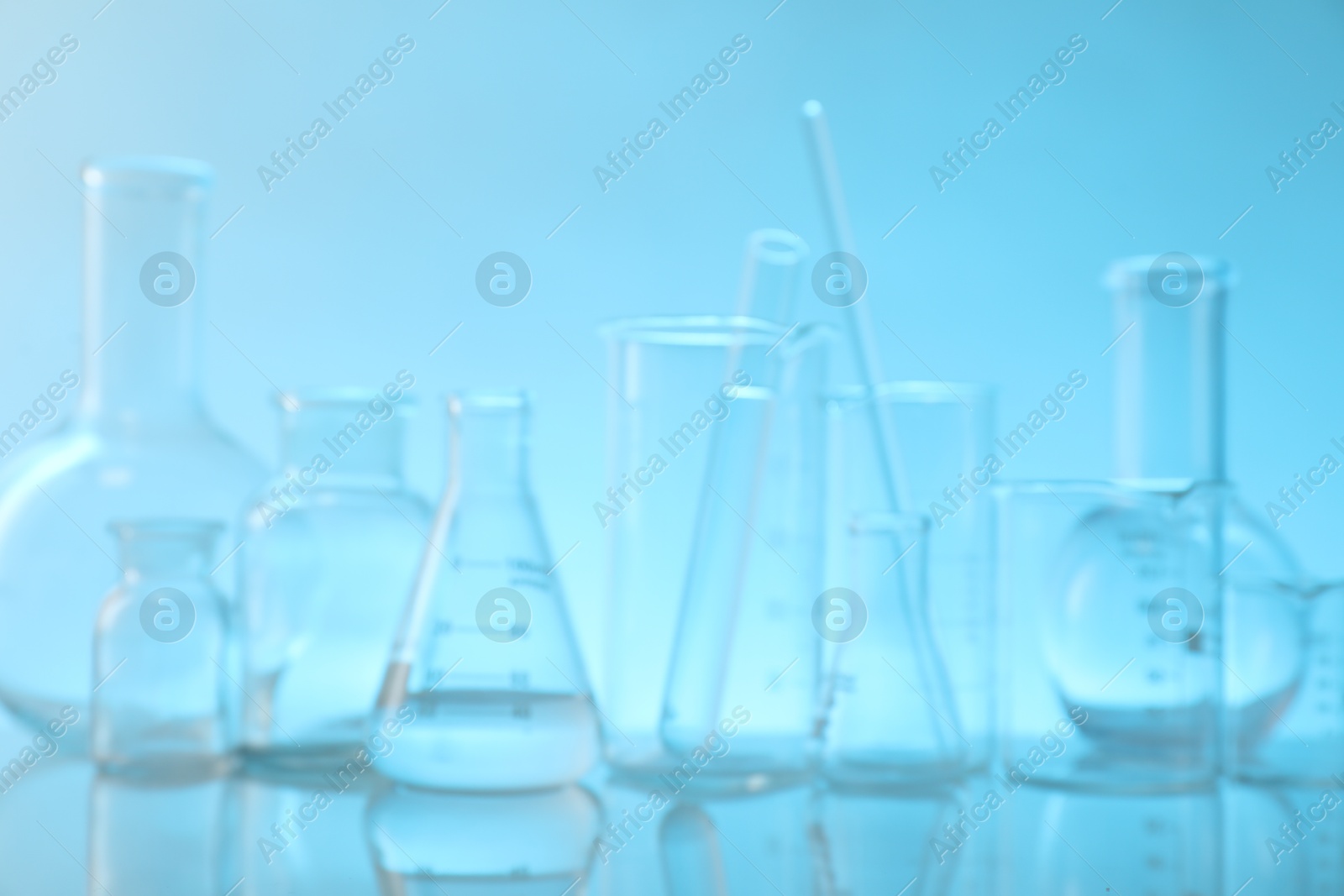 Photo of Blurred view of laboratory glassware on mirror surface against light blue background