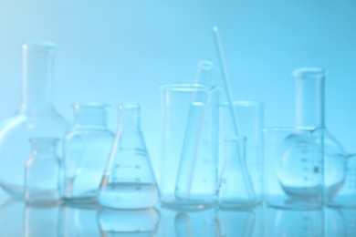 Photo of Blurred view of laboratory glassware on mirror surface against light blue background