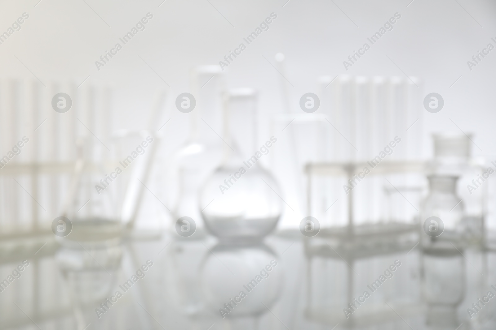 Photo of Blurred view of different laboratory glassware on mirror surface against light background