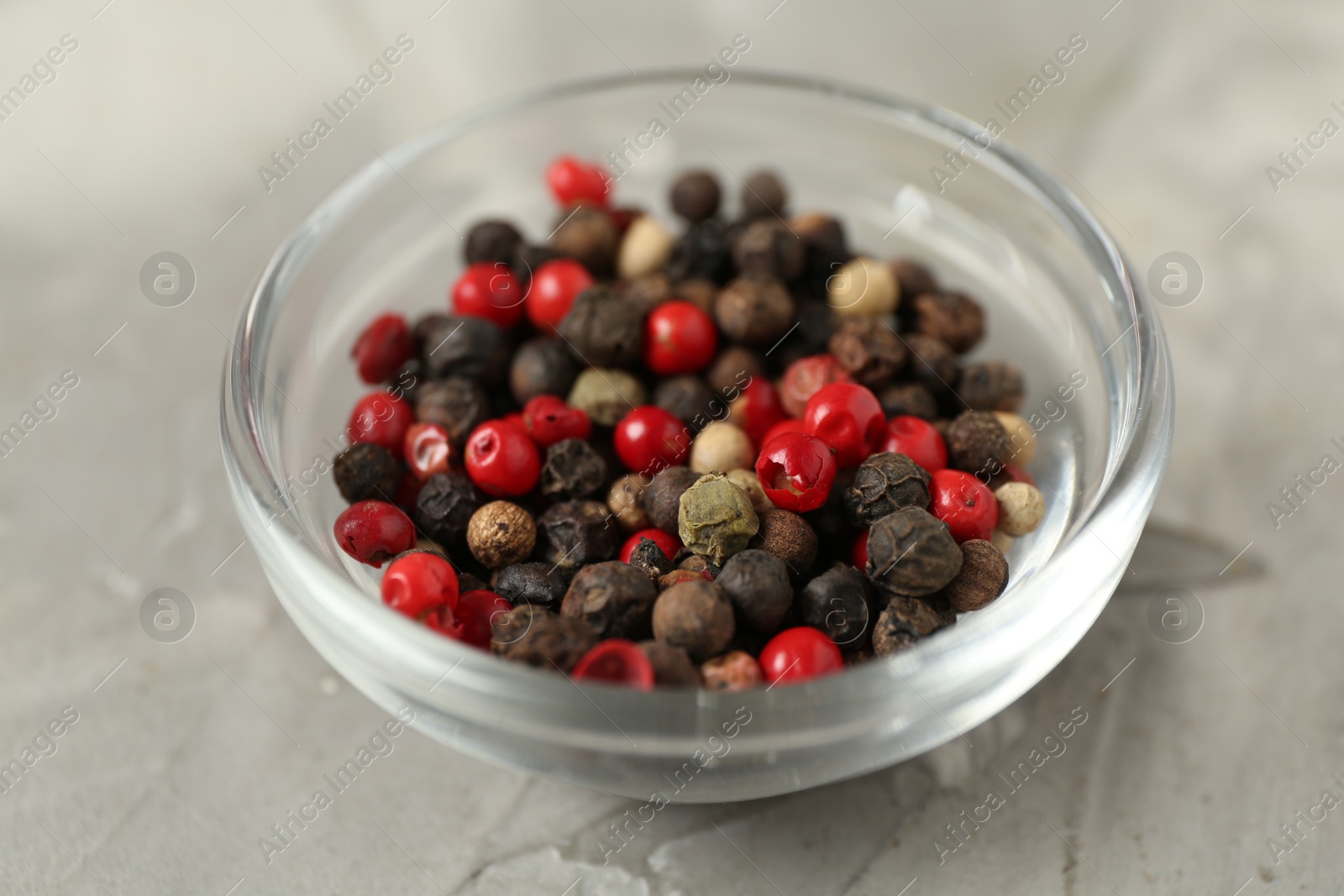 Photo of Bowl of peppercorns on grey textured table, closeup