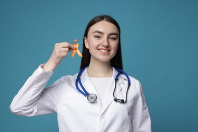 Photo of Multiple Sclerosis awareness. Happy doctor holding orange ribbon on light blue background