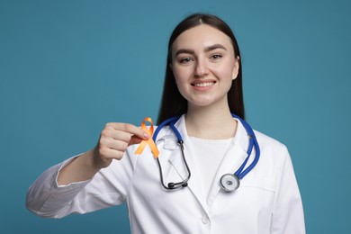 Photo of Multiple Sclerosis awareness. Happy doctor holding orange ribbon on light blue background