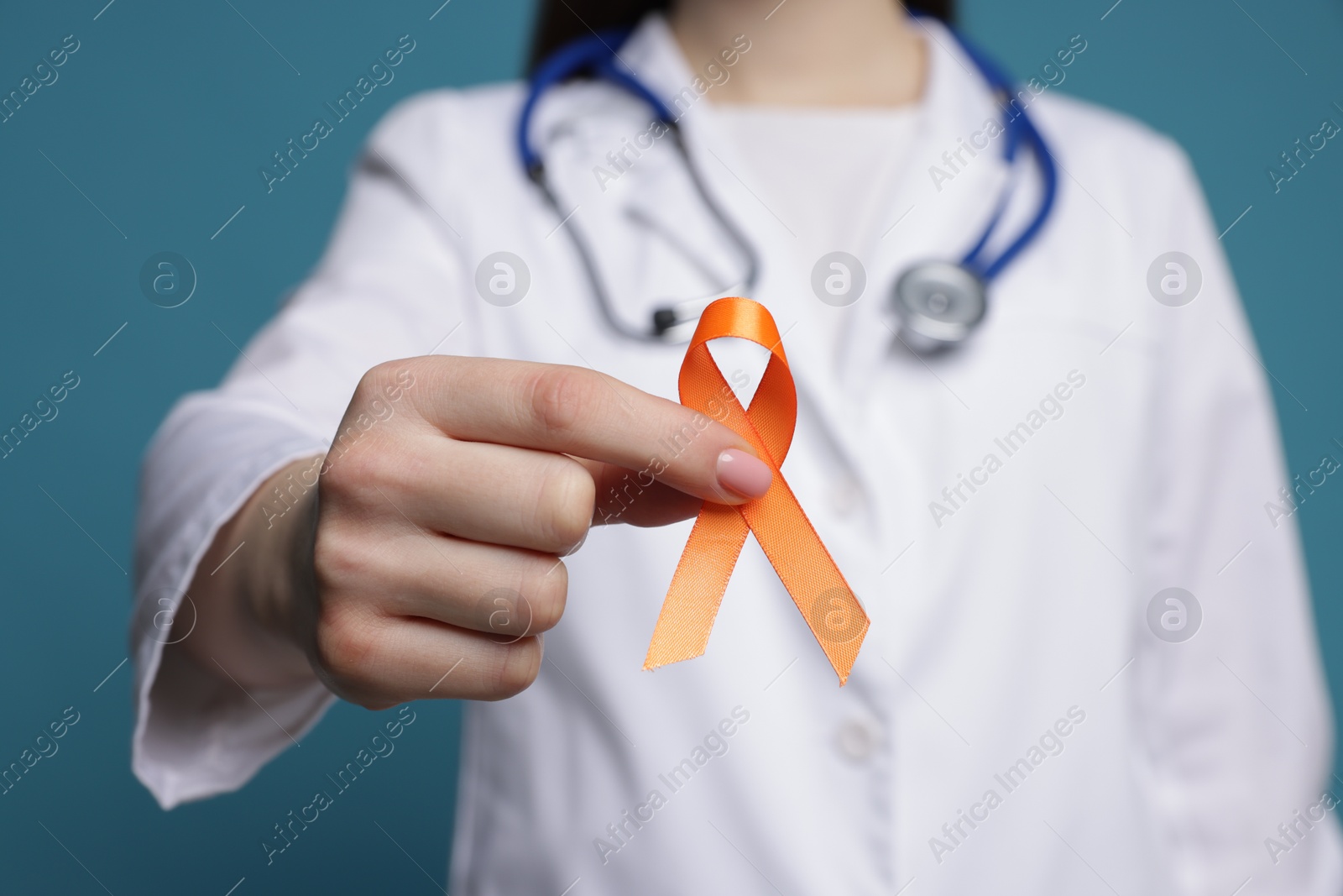 Photo of Multiple Sclerosis awareness. Doctor holding orange ribbon on light blue background, closeup