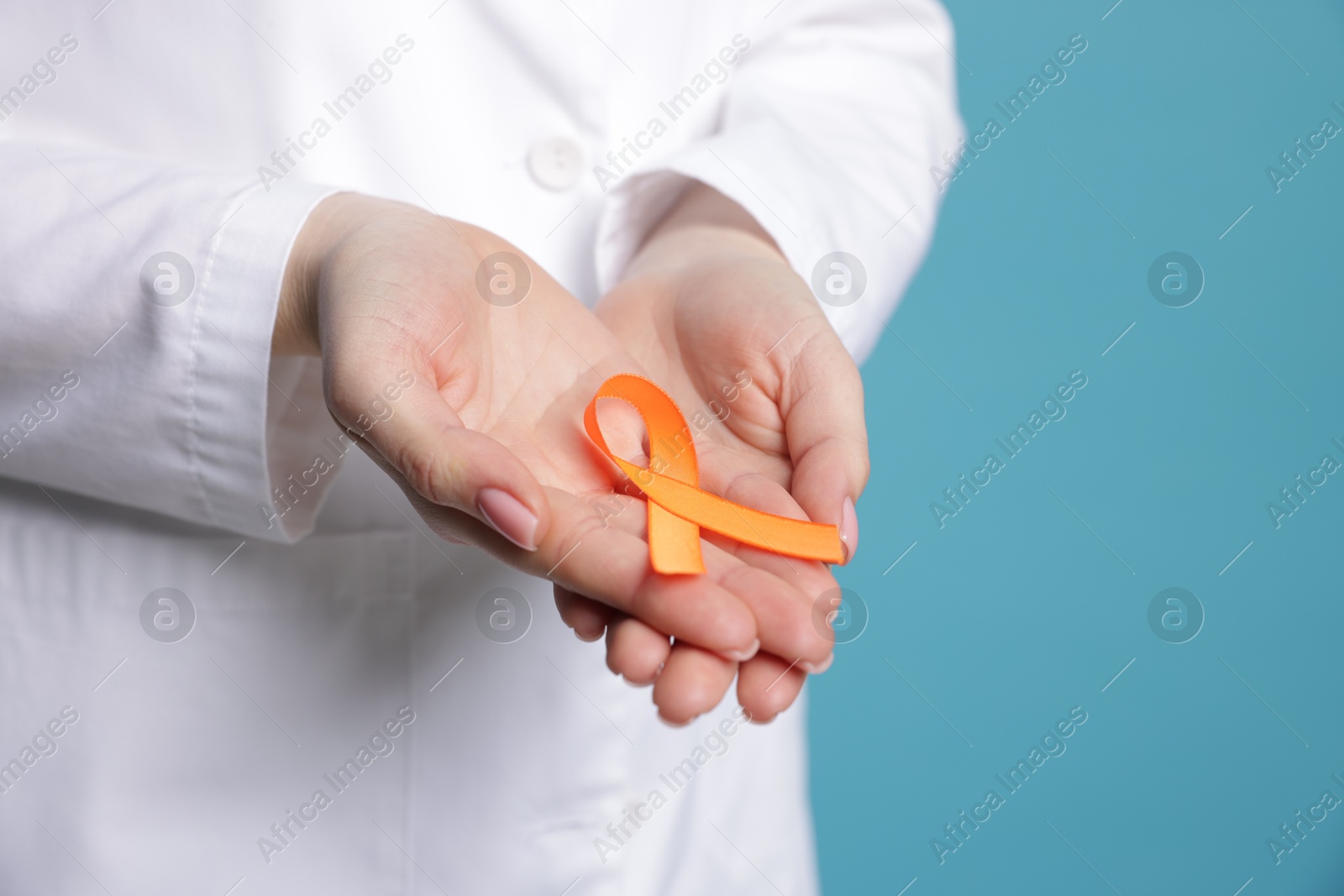 Photo of Multiple Sclerosis awareness. Young woman holding orange ribbon on light blue background, closeup. Space for text