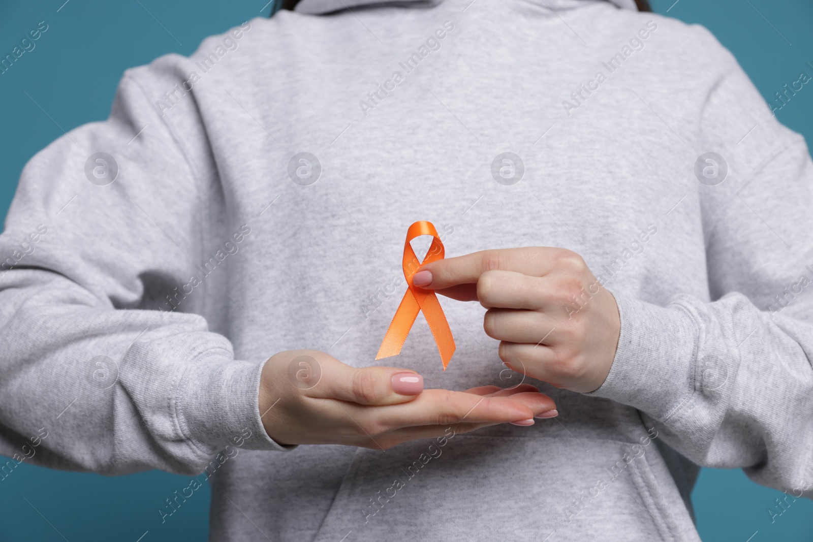 Photo of Multiple Sclerosis awareness. Young woman holding orange ribbon on light blue background, closeup