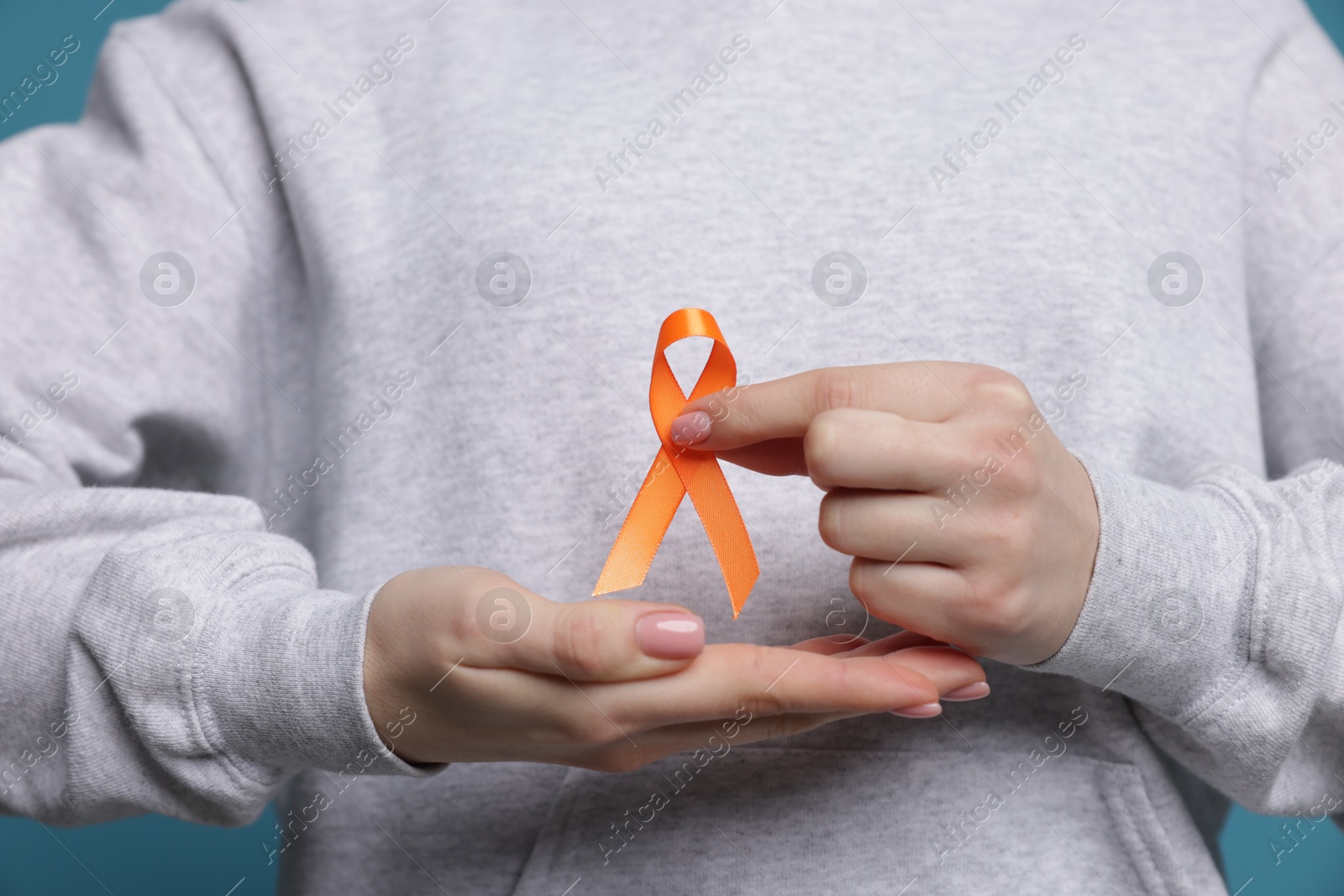 Photo of Multiple Sclerosis awareness. Young woman holding orange ribbon on light blue background, closeup