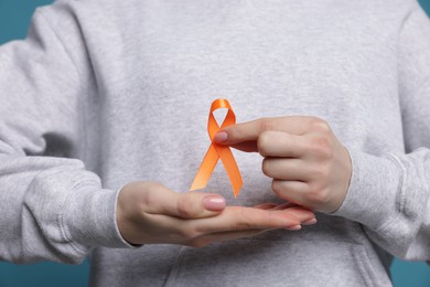 Photo of Multiple Sclerosis awareness. Young woman holding orange ribbon on light blue background, closeup