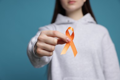 Photo of Multiple Sclerosis awareness. Young woman holding orange ribbon on light blue background, closeup