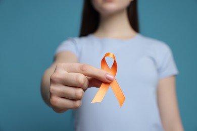 Photo of Multiple Sclerosis awareness. Young woman holding orange ribbon on light blue background, closeup