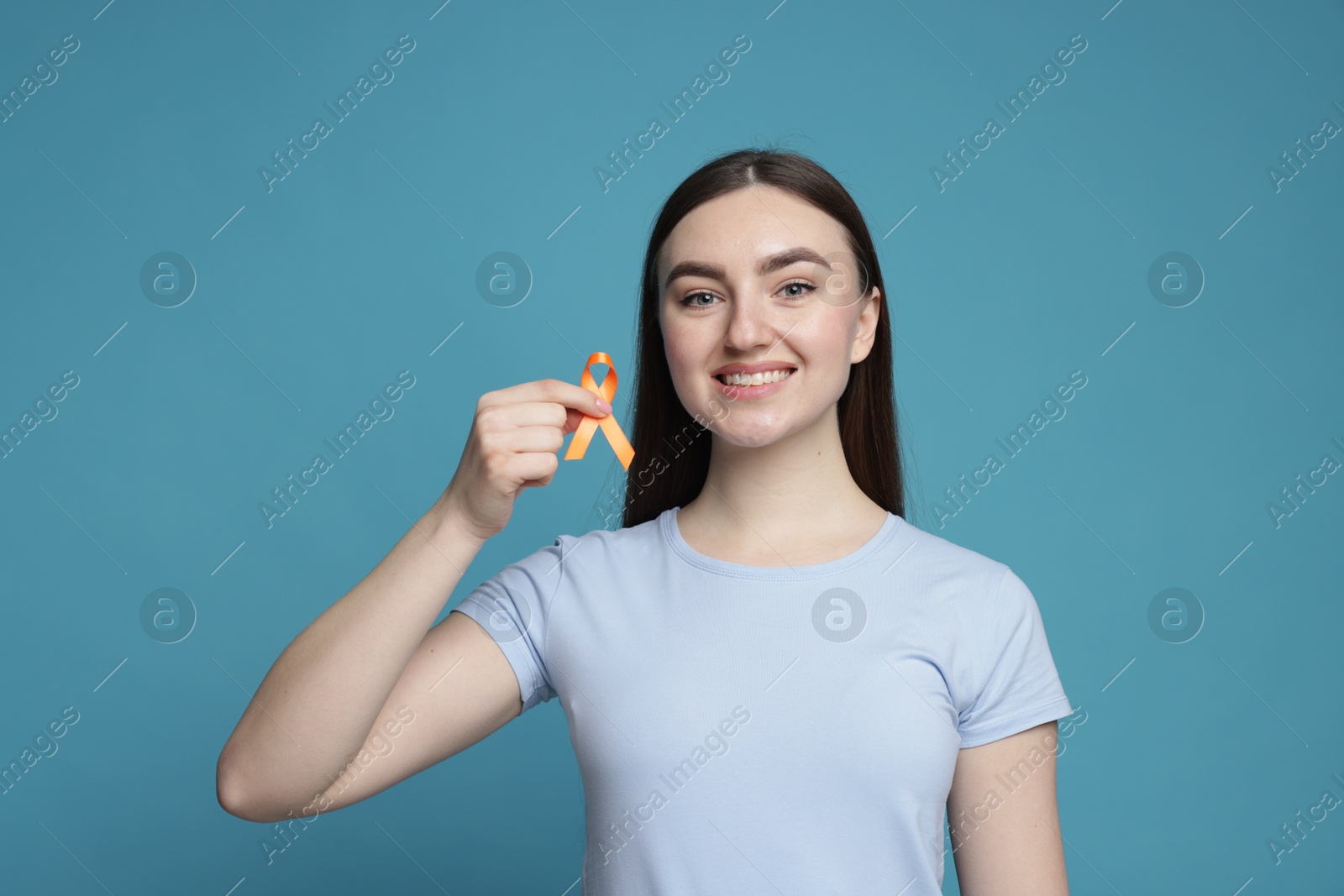 Photo of Multiple Sclerosis awareness. Happy young woman holding orange ribbon on light blue background