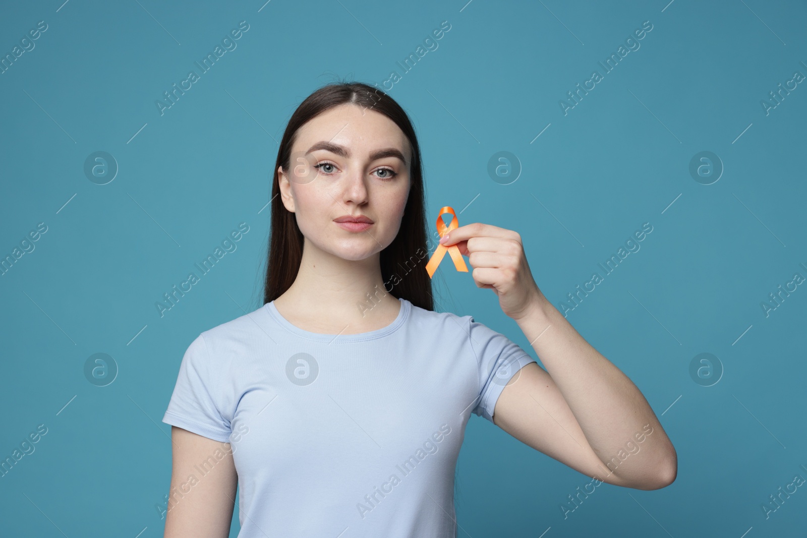 Photo of Multiple Sclerosis awareness. Young woman holding orange ribbon on light blue background