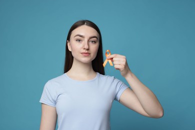 Photo of Multiple Sclerosis awareness. Young woman holding orange ribbon on light blue background