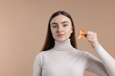 Photo of Multiple Sclerosis awareness. Young woman holding orange ribbon on beige background